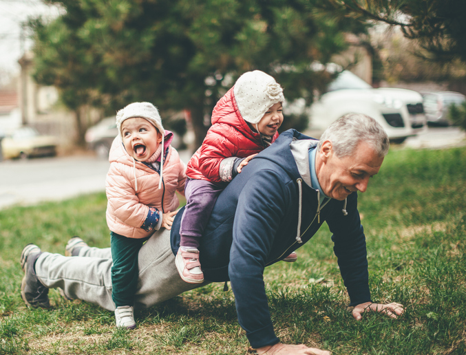 grandfather doing a press-up in the grass with two young grandchildren on his back